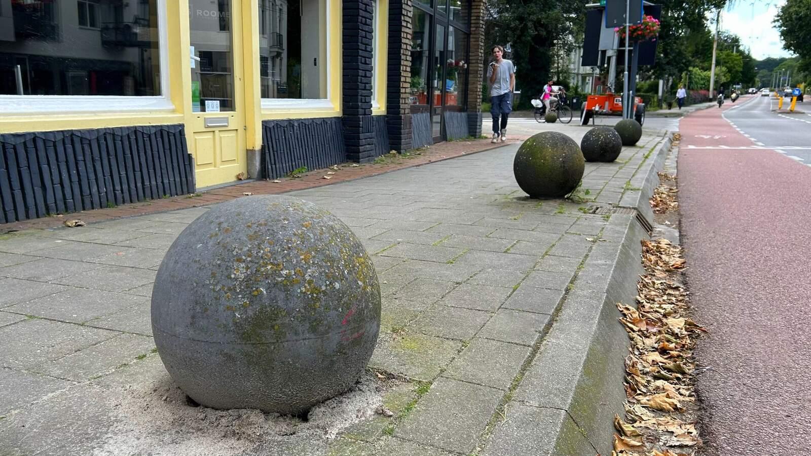 Rangée de boules en béton au bord d'un trottoir, le long d'une rue commerçante