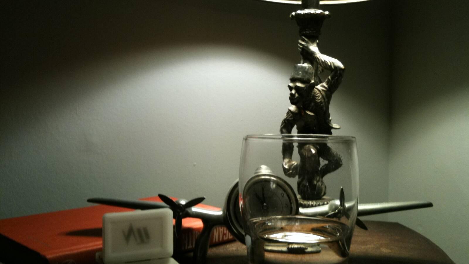 Table de nuit éclairée par une lampe, avec un verre, une montre et un livre, dans une chambre sombre