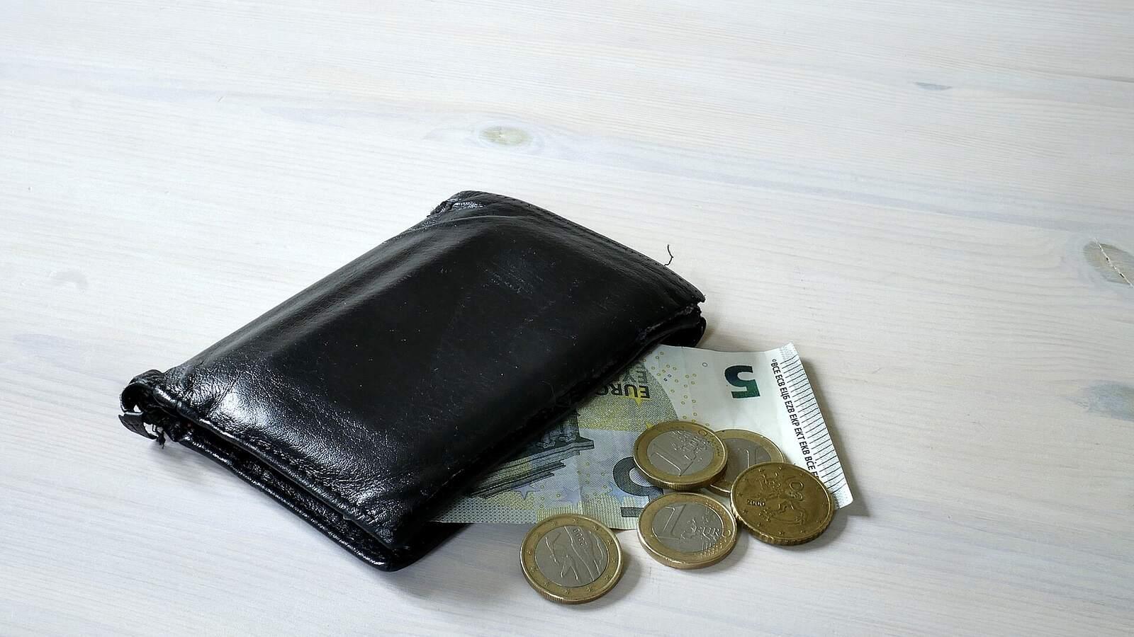 Porte-monnaie en cuir noir posé sur une table, avec un billet de 5 euros et quelques pièces