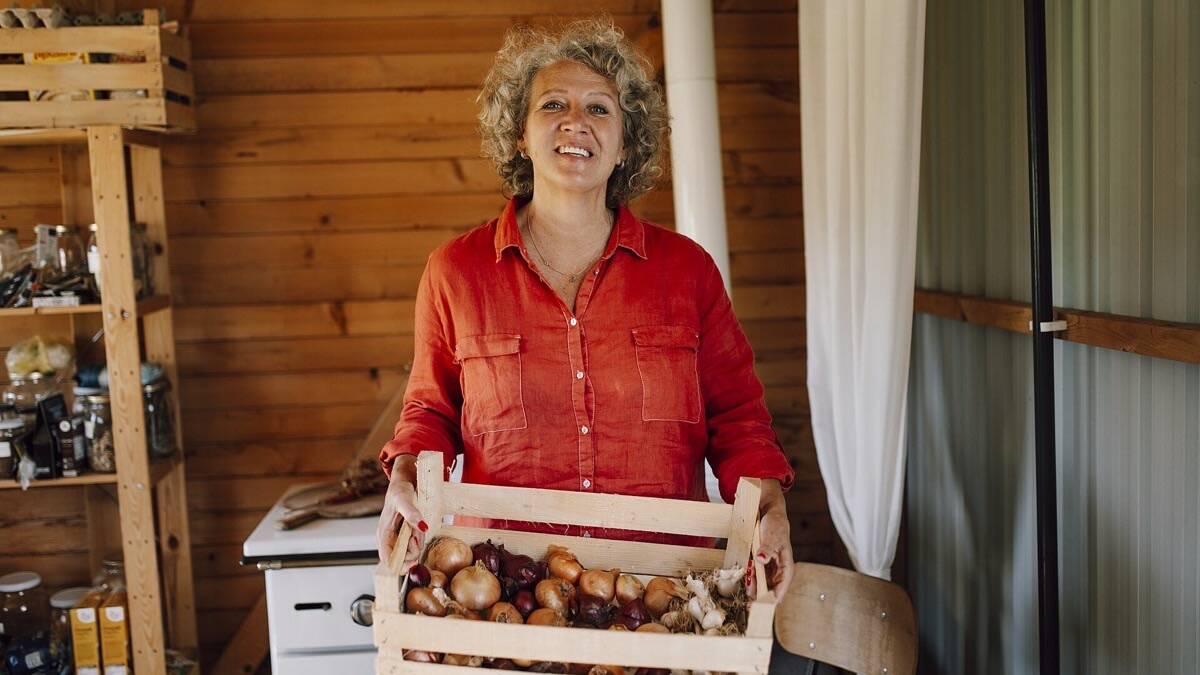 Femme souriante tenant une cagette en bois remplie d'oignons et de légumes du jardin